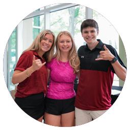 Three students with their arms around each other display the hand sign for spurs up