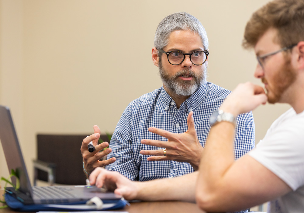 A professor and student looking at a computer and discussing what is on screen.