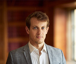 a photo of a man wearing a grey jacket with a white shirt and a dark wood bluured background