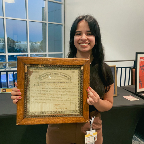 Woman holding a historical medical license in a wood frame.