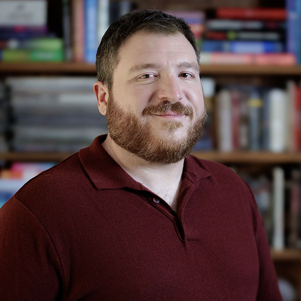 A headshot of script writer Patrick Pianezza in front of a bookshelf